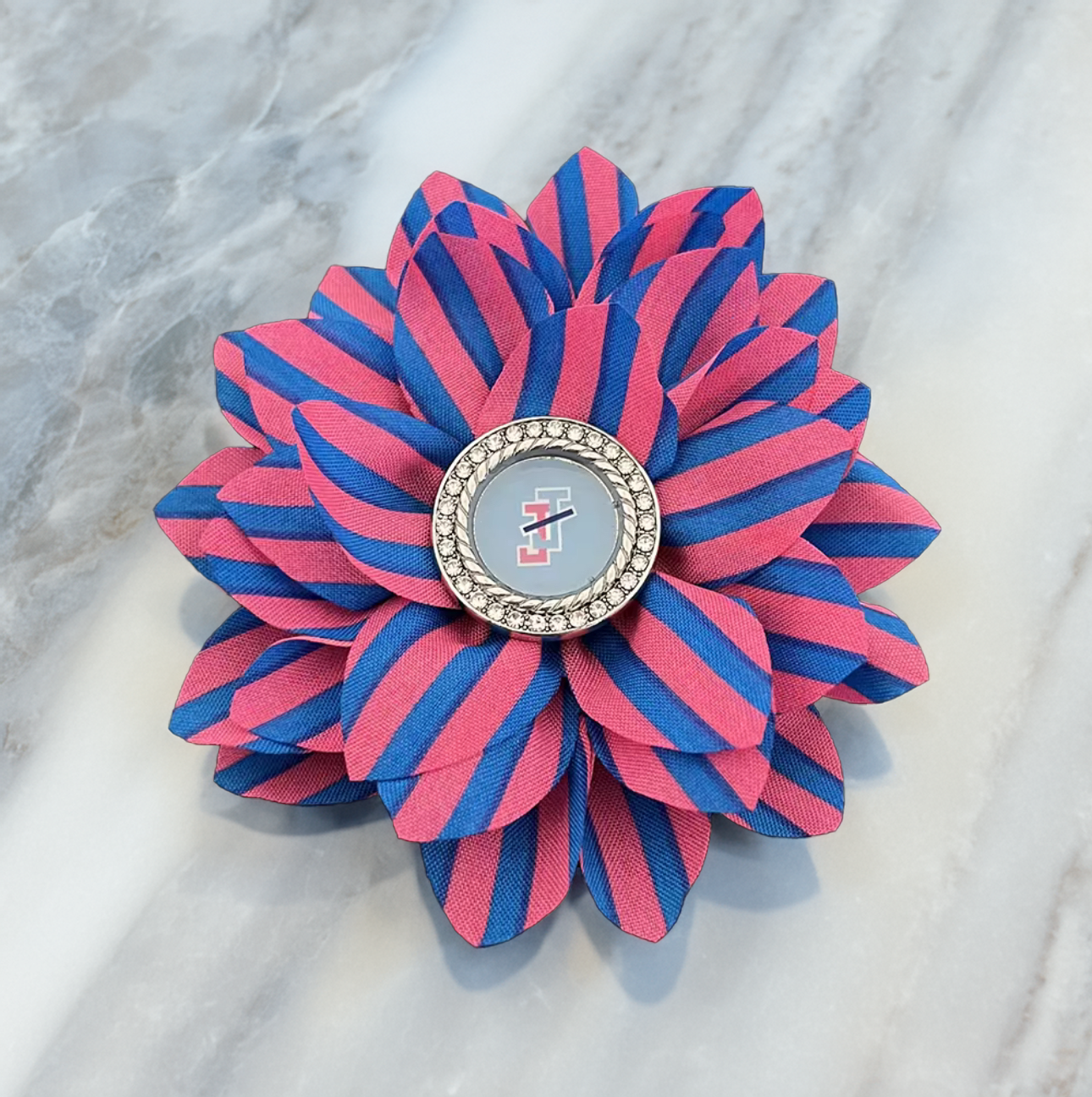 jack and jill of america Pink and blue striped ribbon flower brooch with JJ logo and a rhinestone center shown on a marble table