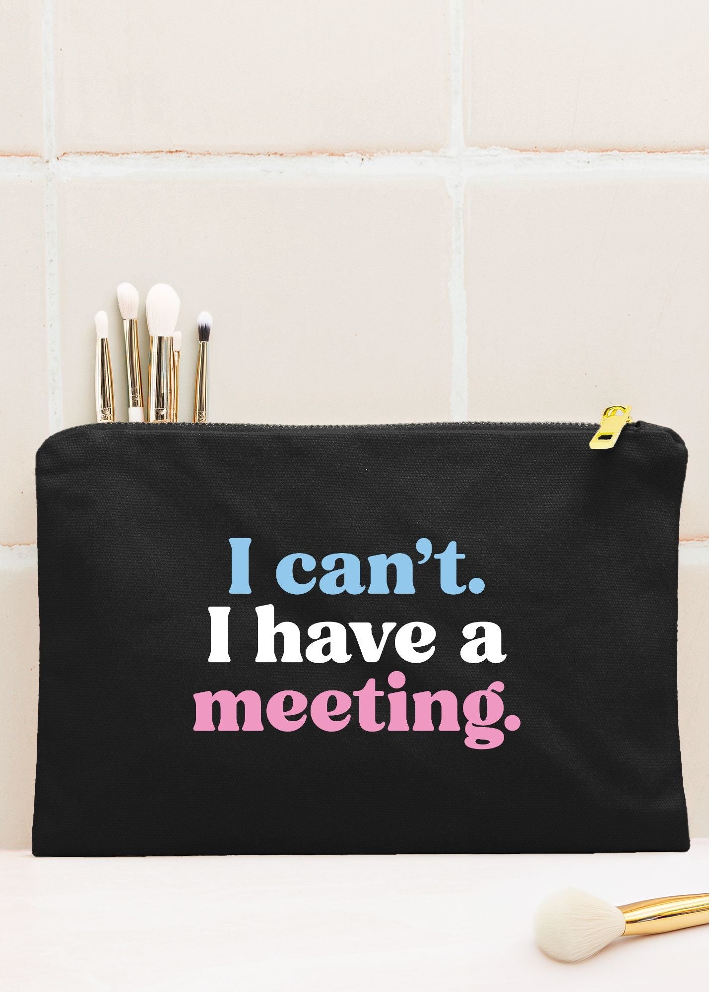 A black cosmetic pouch with a gold zipper and the text 'I can't. I have a meeting.' for Jack and Jill of America mom gifts that can be used as a makeup bag, pencile case, tech case or cosmetic pouch
