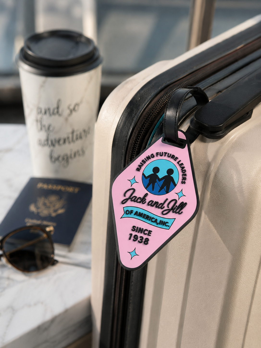 Luggage tag with 'Jack and Jill of America, Inc.' design on a suitcase with travel items in the background.