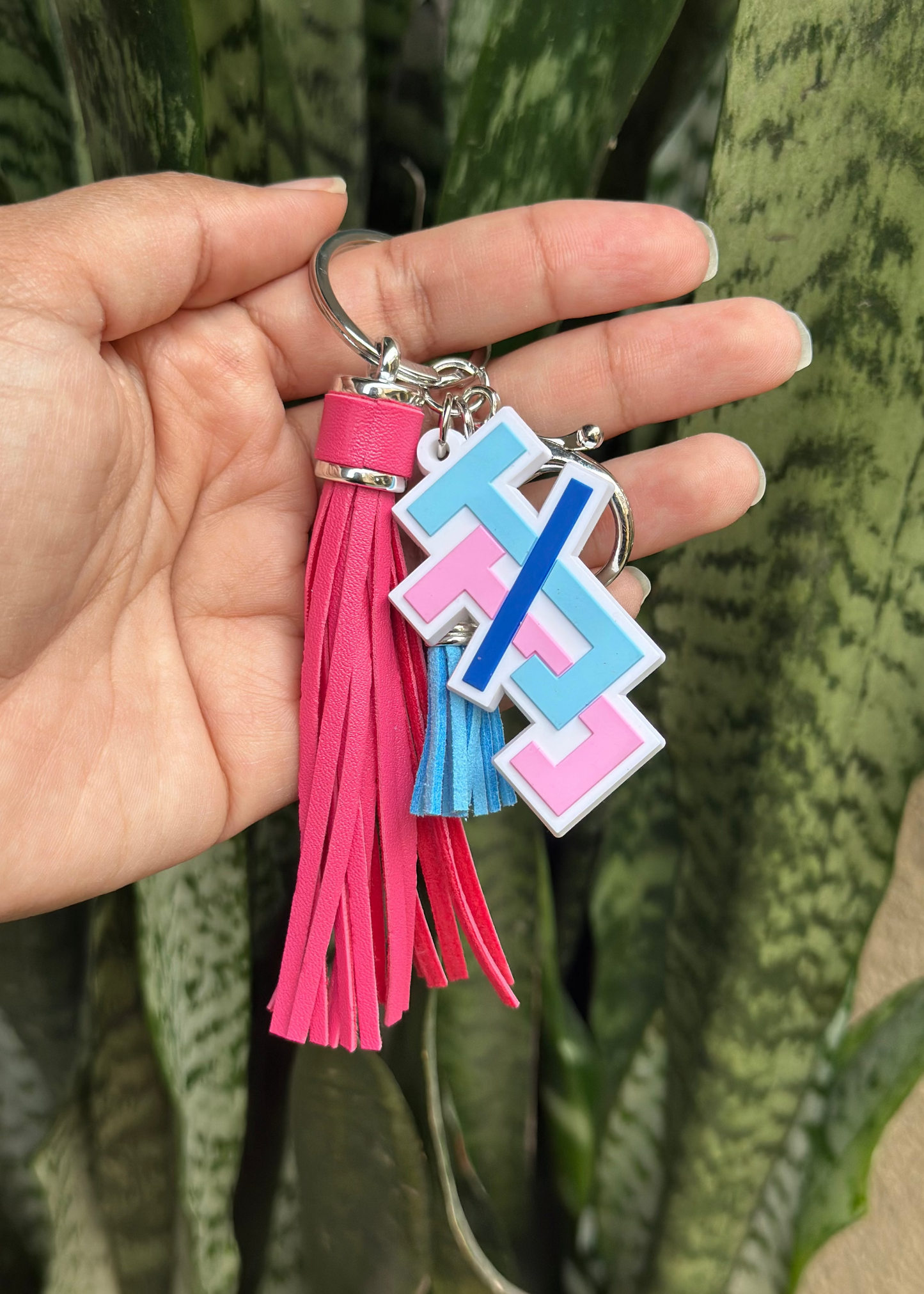 Keychain with pink tassel held by a hand against a green plant background