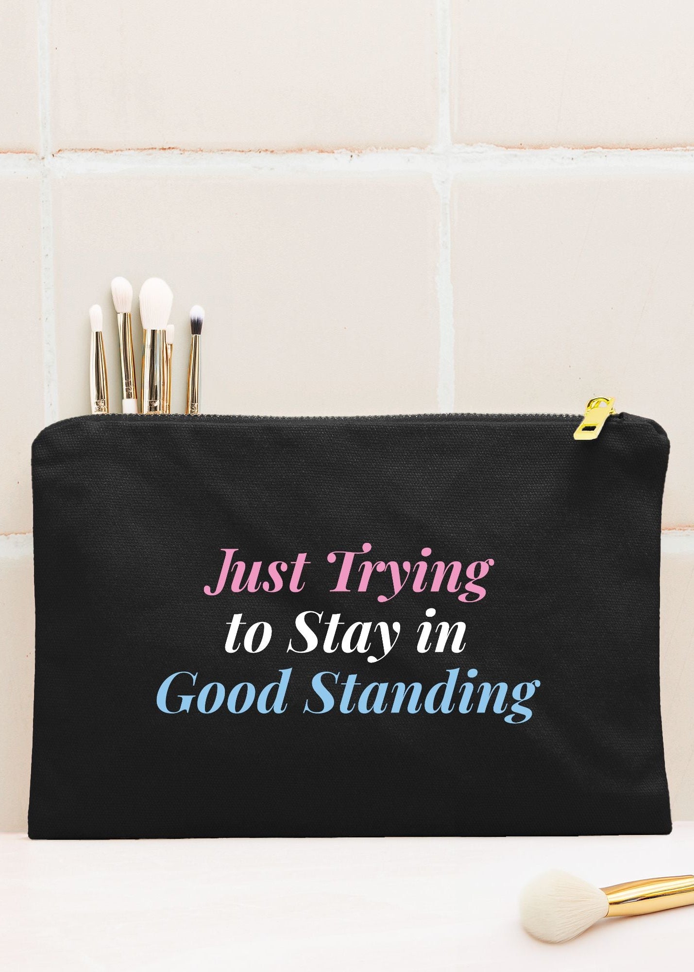 A black cosmetic pouch with a gold zipper and printed text reading 'Just Trying to Stay in Good Standing' in pink, white, and blue for Jack and Jill of America mom gifts
